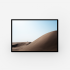 A framed photograph of sand dunes with a car and people in the distance.
