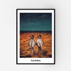 Framed wall art of two zebras standing in an orange field looking at a blue stormy sky. The framed art includes white border with text saying 'Namibia'