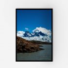 A framed photo of a glacier, laker and a mountain range under a clear blue sky.