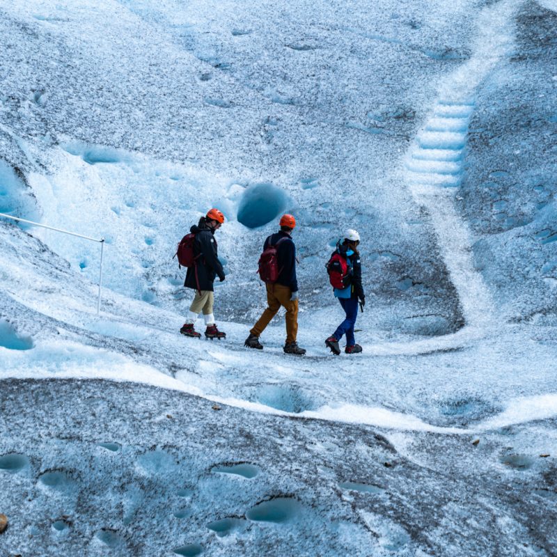 three people walking on ice on a glacier