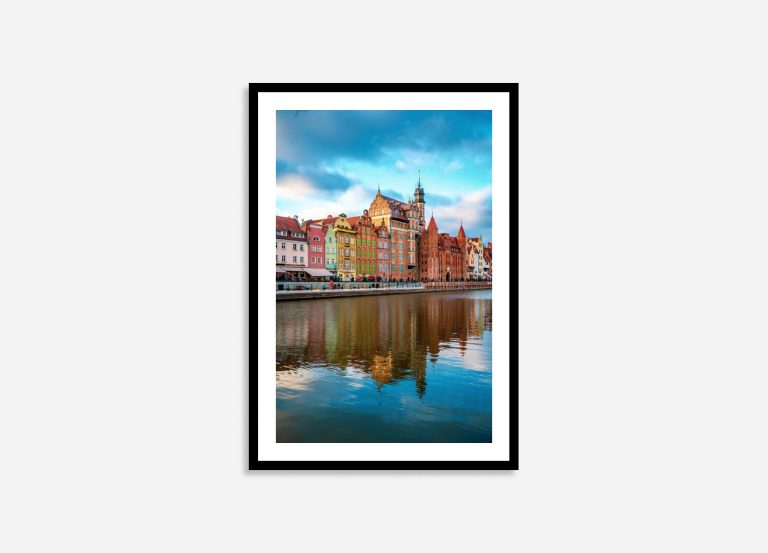 Colorful historic buildings line a charming Gdansk street, their vibrant facades mirrored perfectly in the calm river under soft sunset light.