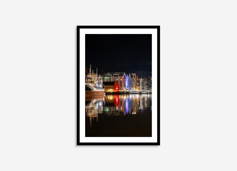 Night view of Gdansk, Poland featuring a brightly lit buildings and ships docked by the waterfront, and colorful reflections on the water.