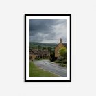 A tranquil scene of a Cotswolds village featuring traditional English stone cottages, verdant trees, and a winding road, all set against an overcast sky.