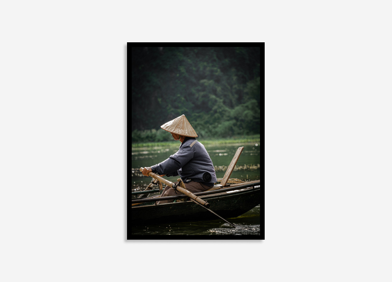 Vietnamese man rowing a boat, wearing a traditional conical hat on the wate